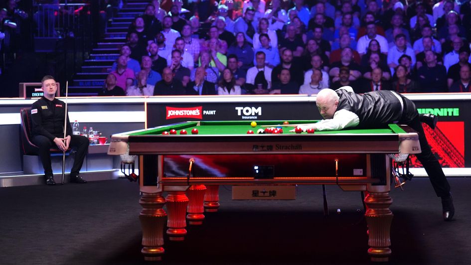 John Higgins at the table as Kyren Wilson watches on