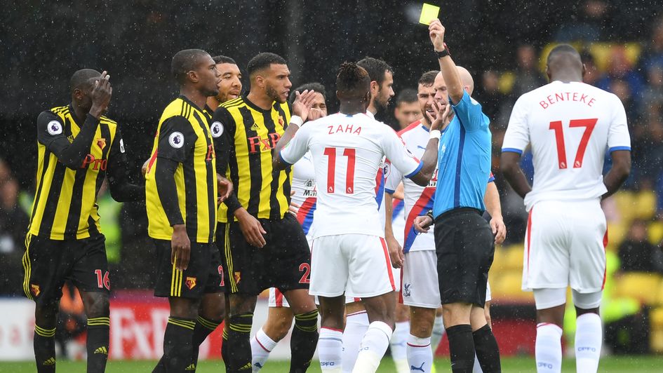 Wilfried Zaha is shown a yellow card by referee Anthony Taylor during Watford v Crystal Palace