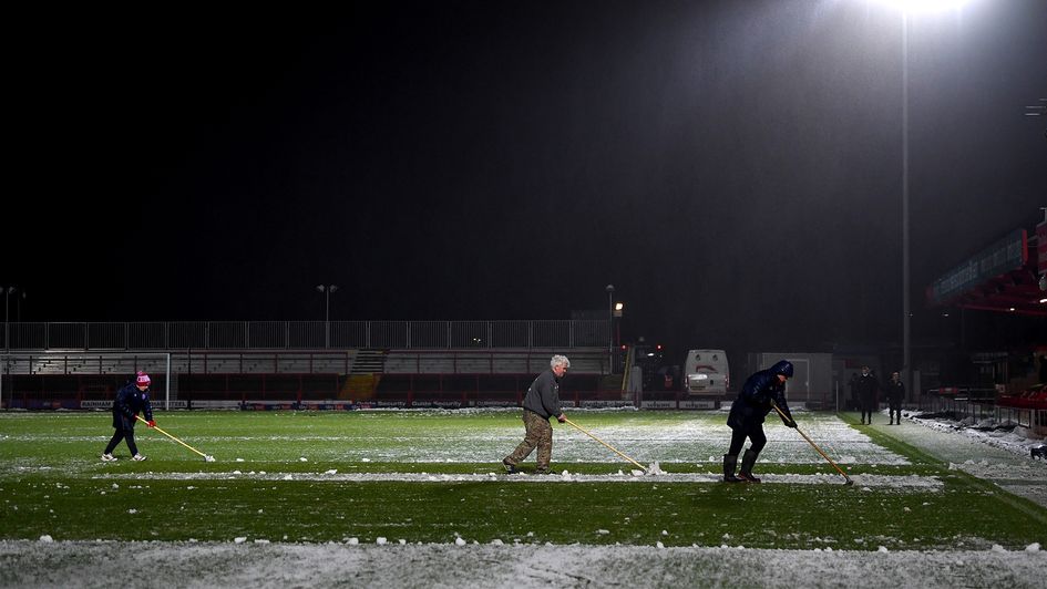 Ground staff clear the snow off the pitch